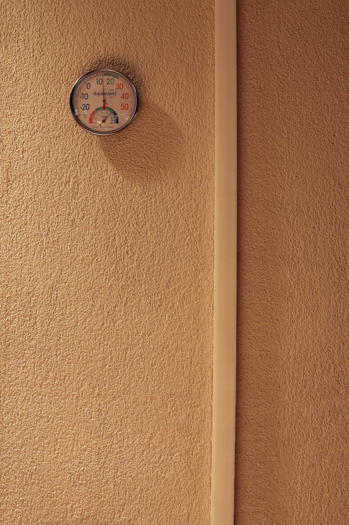 A minimalist indoor scene featuring a hygrometer mounted on a textured wall, indicating temperature and humidity.