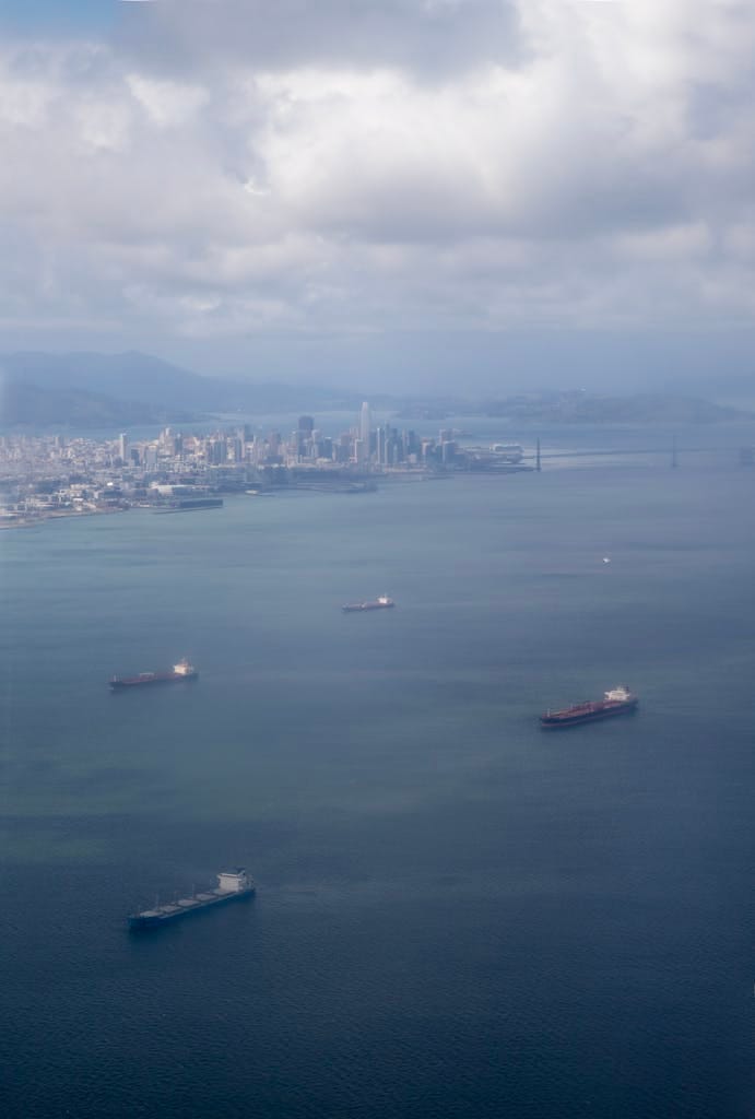 Aerial shot of cargo ships in San Francisco Bay with city skyline and iconic bridge in the background.