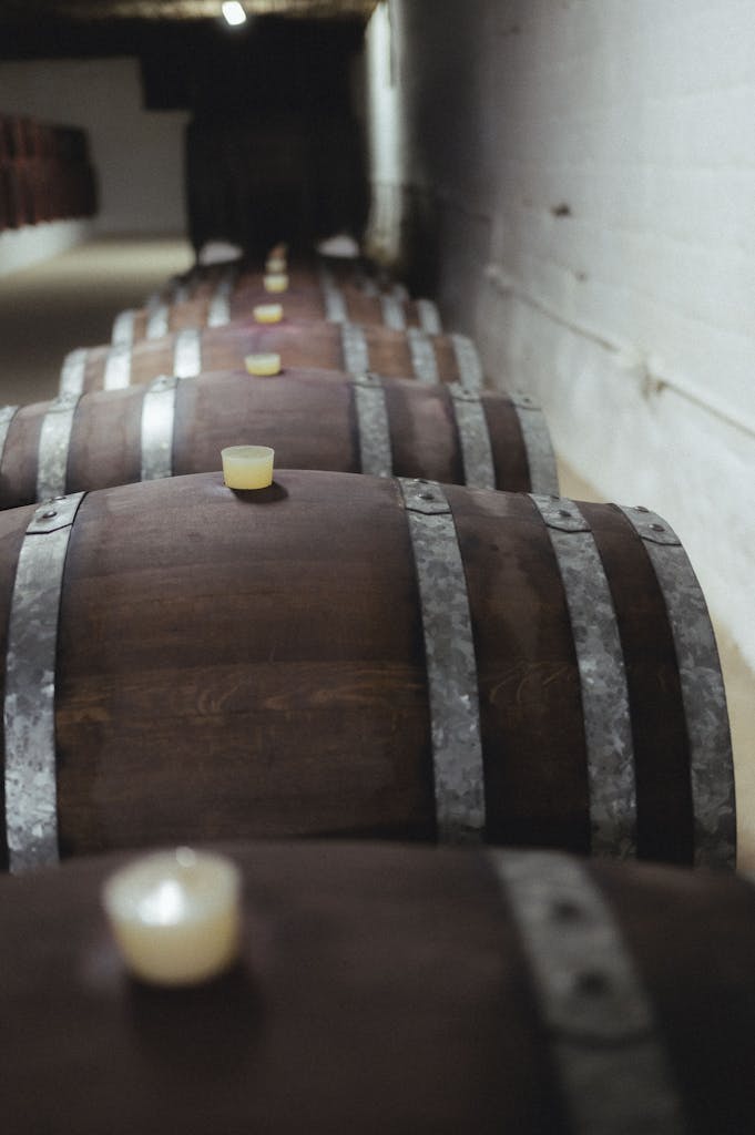 Long row of wooden barrels in a dimly lit winery cellar with candles on top.