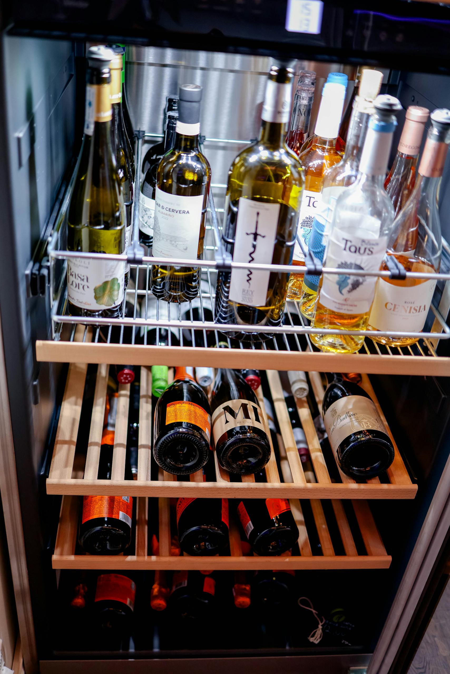 Variety of wine bottles stored in a cooling fridge with organized wooden racks