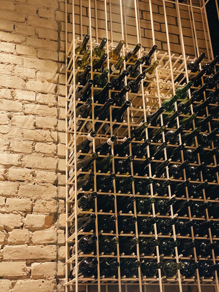 Vertical shot of neatly organized wine bottles in a rustic brick wine cellar.